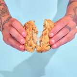 Hands breaking apart a chunky stuffed Bueno New York Cookie with gooey white chocolate hazelnut filling.